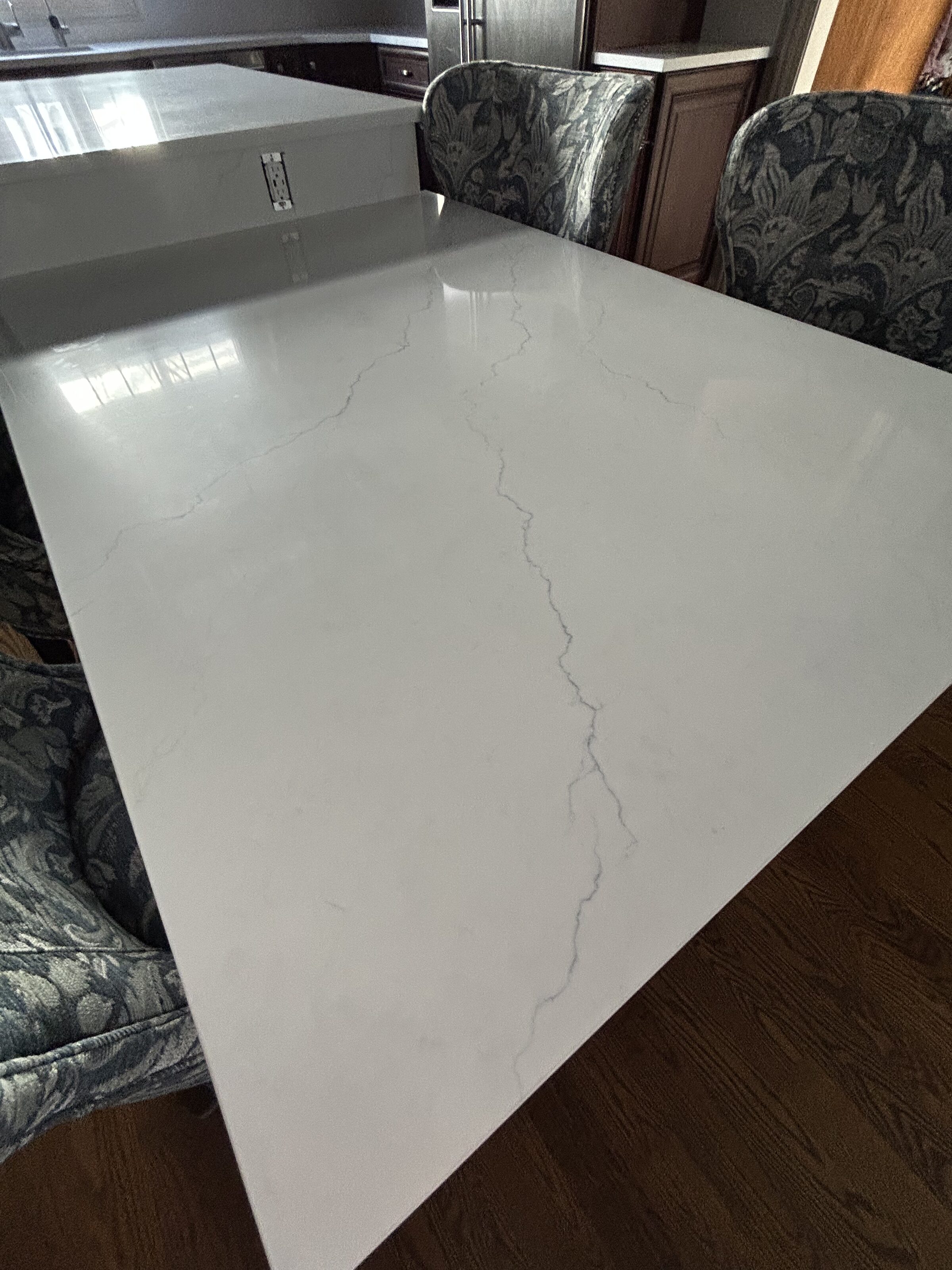 Finished white quartz island with a soft gray vein, cherry cabinets behind it and a pressed-tin ceiling overhead