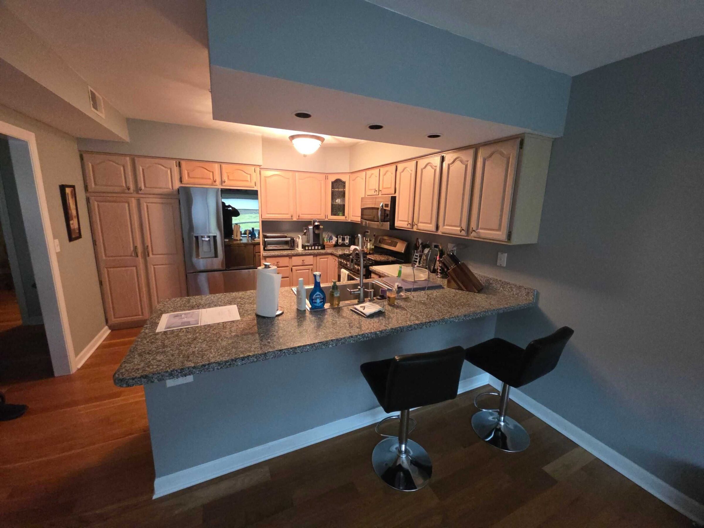 The old pickled oak kitchen with its brown granite peninsula and two black stools
