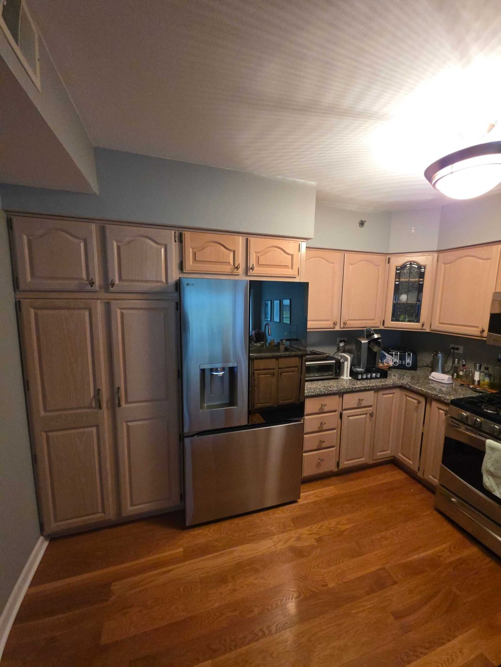 The same room before, pickled oak cabinets and granite counters under a dropped bulkhead