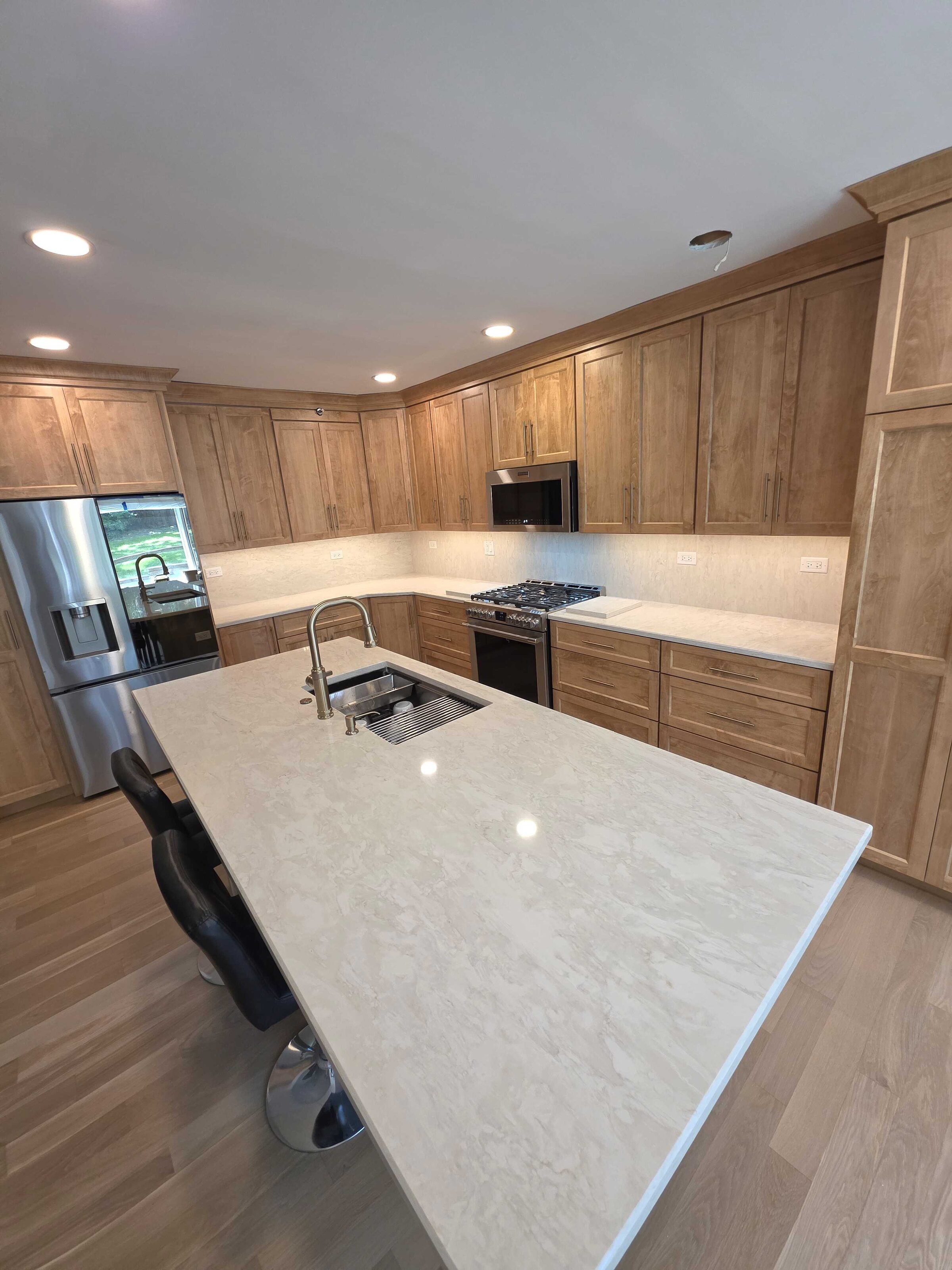 Long cream quartz island with seating, in a newly built light maple kitchen