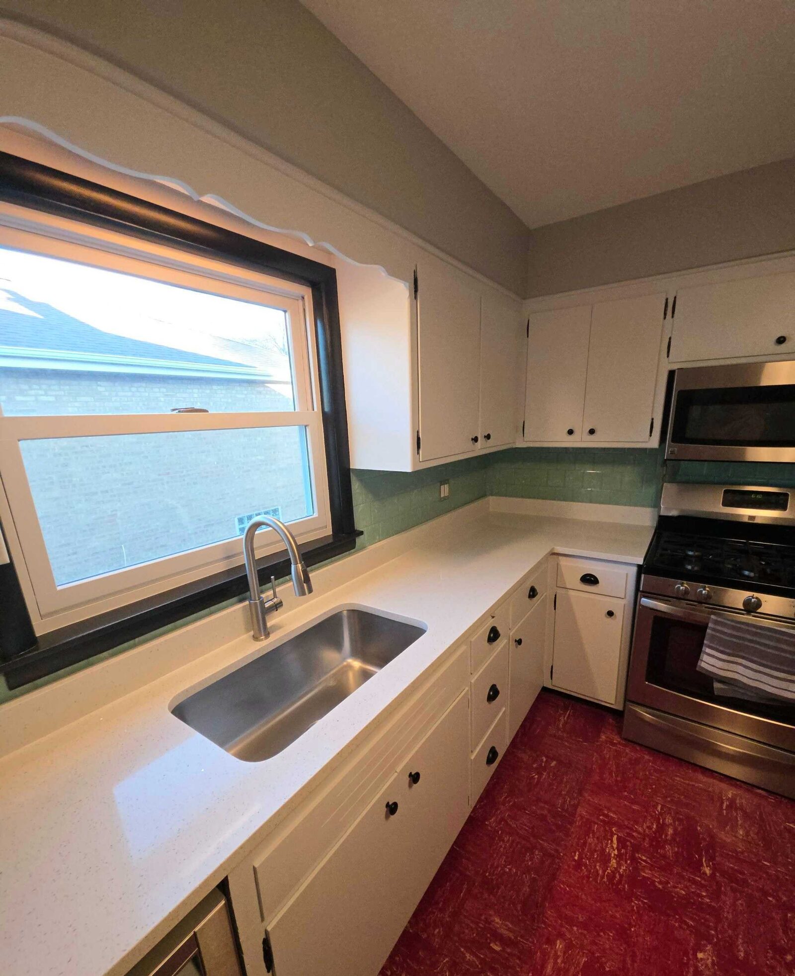 Finished white counter running under the window to a new stainless sink, mint tile behind and red floor below