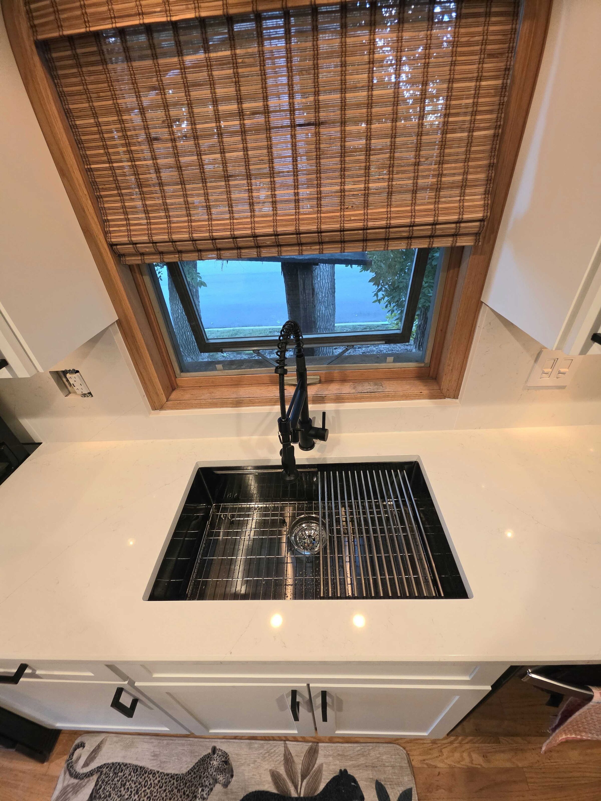 Black composite undermount sink and matte black faucet set into new white quartz under the window